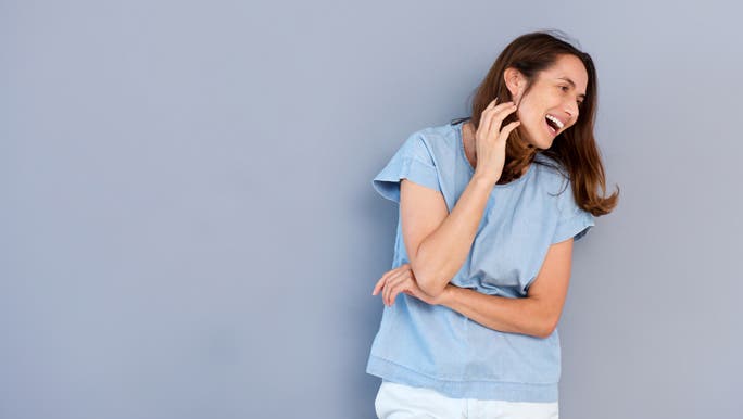 Mid age woman laughing in front of a grey wall