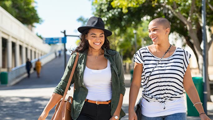 Two friends walking outside smiling and laughing as they do 10,000 steps and wonder how many steps are in a km. 