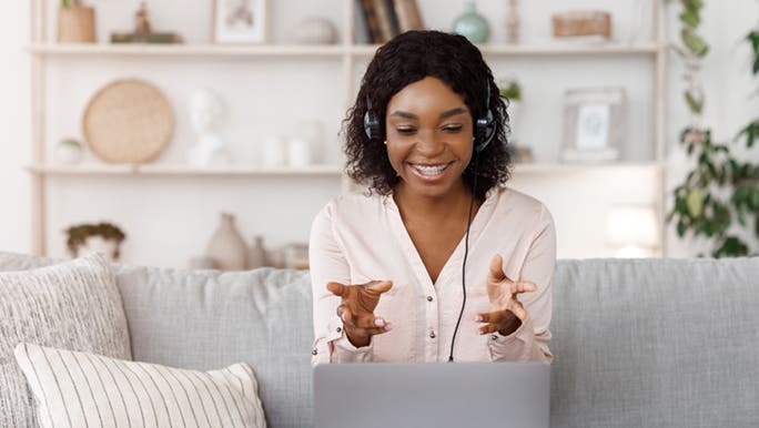 A life coach sits on a lounge, she is smiling and explaining to a client different strategies they should try. She has her hands out as if caught mid-sentence. 