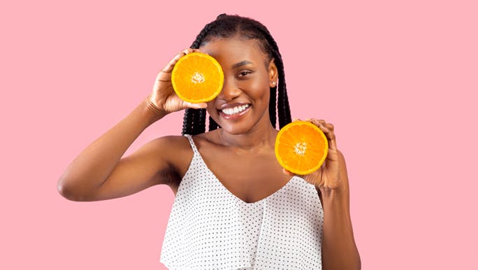A woman in front of a colourful background holds up half a citrus fruit and wonders whether low iron can cause digestive problems.
