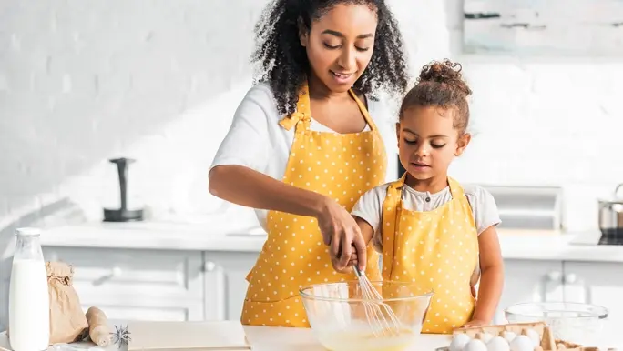 Mother and daughter in matching yellow aprons with white polka dots whisking baking ingredients