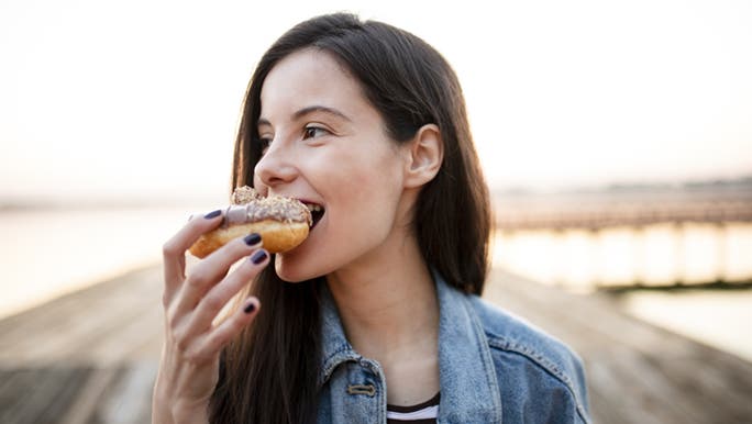 A lady is looking to the side as she happily bites into a donut. 