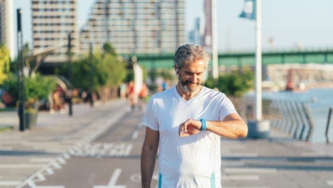 Man smiling as he is walking and looking at his fitness track to work out many steps per day he has taken. 