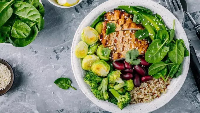 Healthy buddha bowl with grilled chicken, quinoa, spinach, avocado, brussel sprouts, broccoli, red kidney beans and sesame seeds