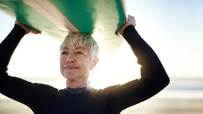 Woman holding a green surfboard on top of her head on her way to go surfing