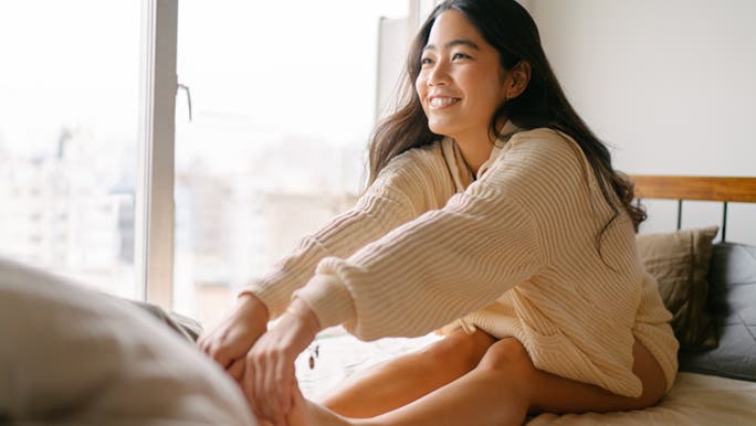 A lady is holding her toes in a sun drenched bedroom. It looks as though she is enjoying her morning stretch. 