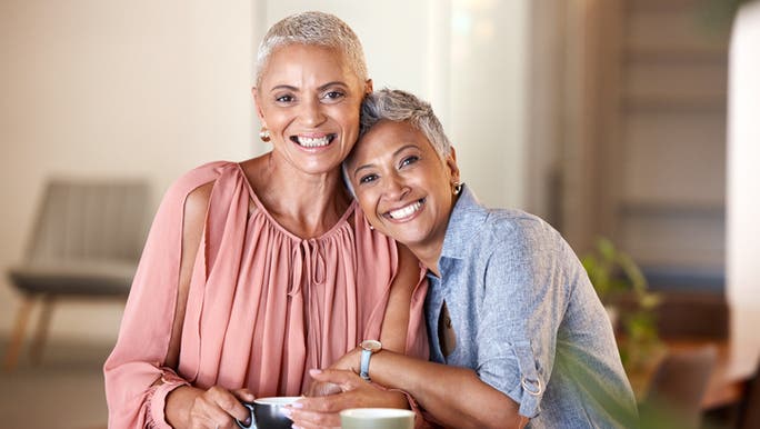 Two women are drinking coffee and smiling as they share a hug