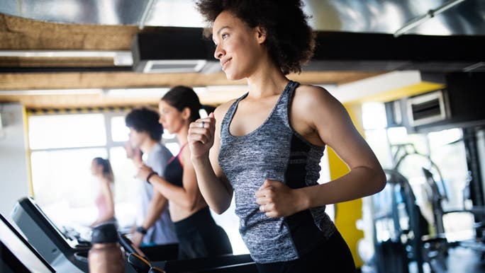 A woman smiles while running on a treadmill with others in the background at an altitude training gym.