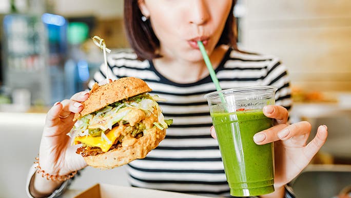 A lady holds a burger in one hand and a green smoothie in the other. It’s called balance. 