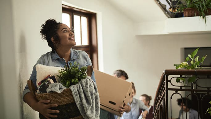 A family is walking up stairs carrying baskets and boxes in a light-filled building. They seem excited about moving house. 