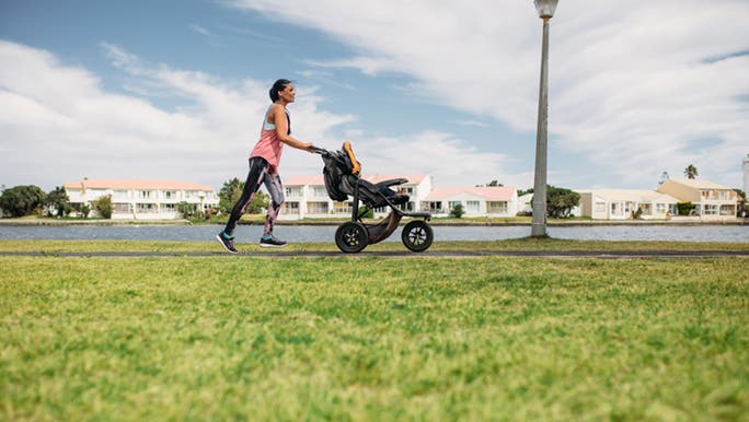 A woman is enjoying the benefits of jogging with her child in a pram.