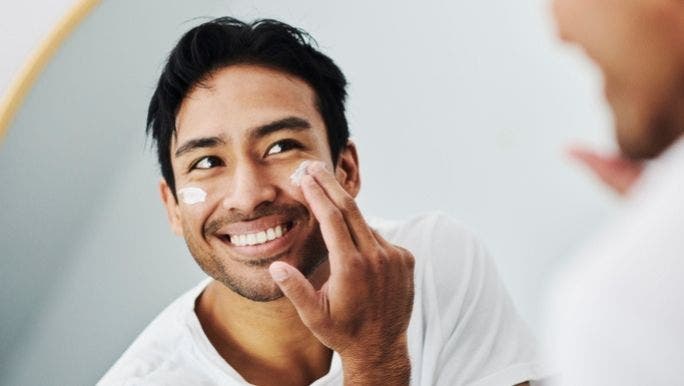 A man looks in a mirror while he applies moisturiser cream to his face