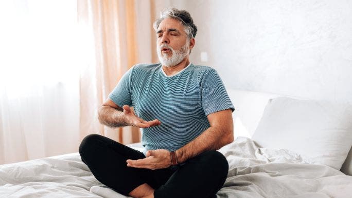 A middle-aged man practising deep breathing on a bed