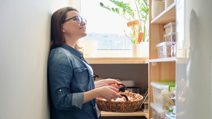 A woman wearing glasses is organising a small pantry