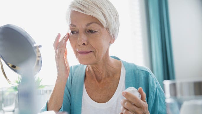 A senior woman is looking into a mirror and applying face cream