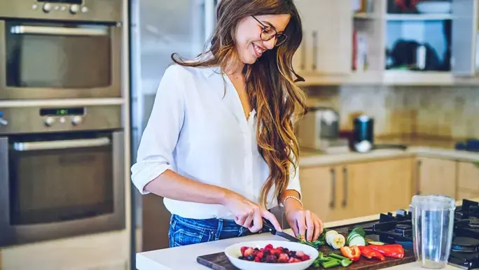 Woman in jeans and a white shirt preparing a low FODMAP vegetable and fruit smoothie
