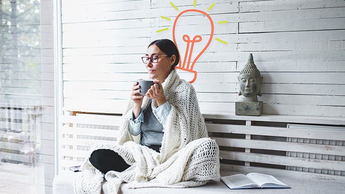 Woman in her 40s relaxing with a cup of tea. Her eyes are closed and she is wrapped in a shawl