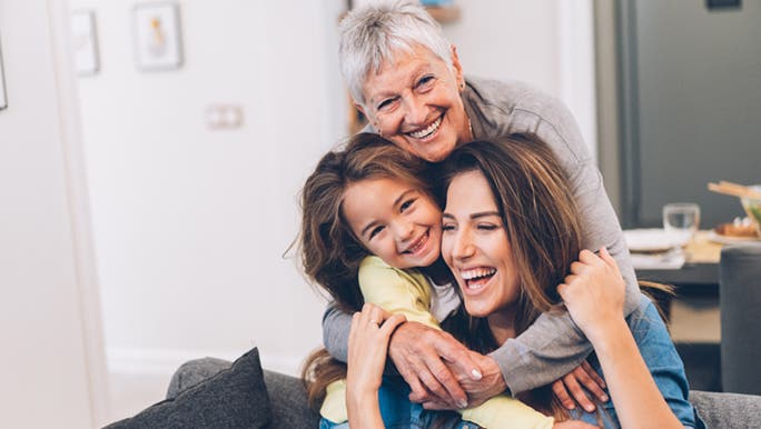 A child and grandmother hug a woman who is part of the sandwich generation. 