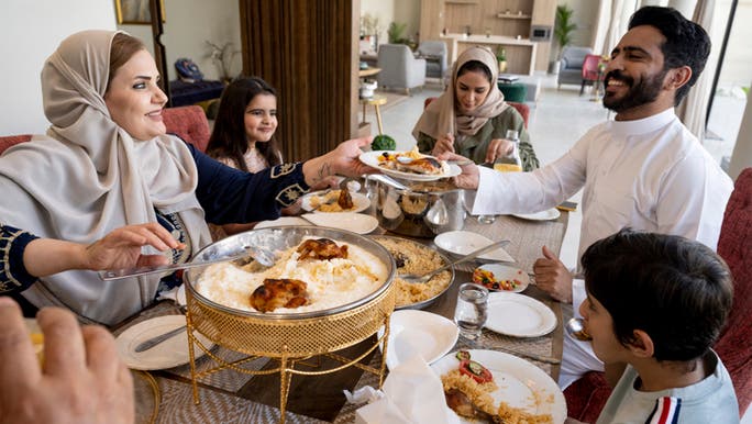 A large Middle-Eastern family are smiling and sharing a meal around a dinner table