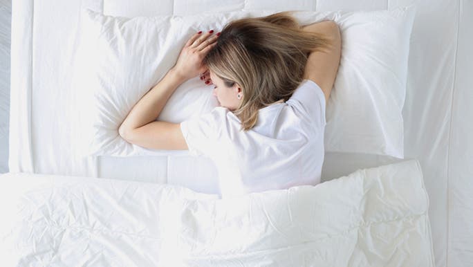 A young woman is sleeping on her stomach in a white bed