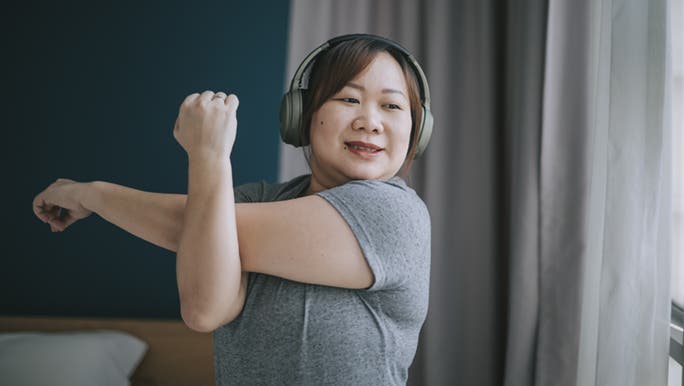 Lady wearing headphones stretching before exercise to prevent muscle injuries. 