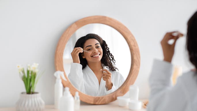 Looking happily into the mirror, a woman in Australia is applying the best face serum for her