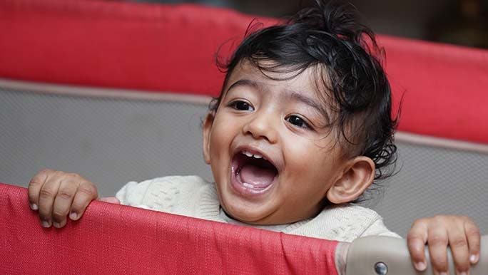 Toddler smiles from their crib at their parents who are thinking about how many baby teeth will grow. 