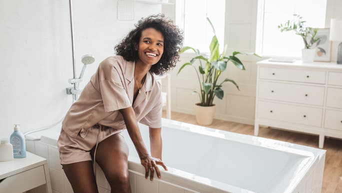 A young woman is sitting on the edge of a bath and smiling
