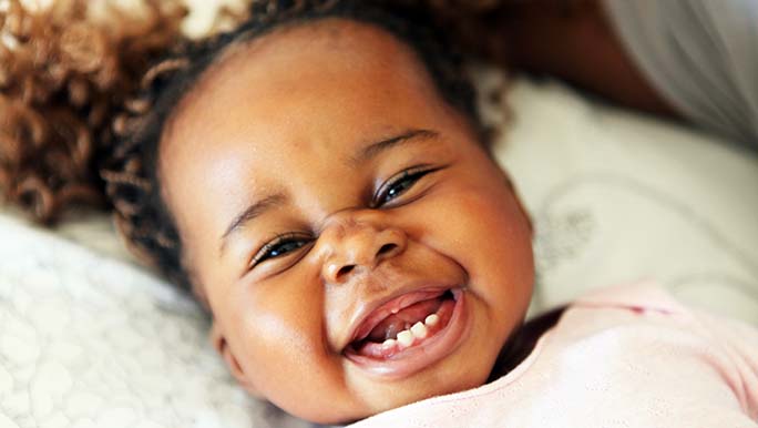 Baby girl smiling while her parents wonder when to start brushing baby teeth