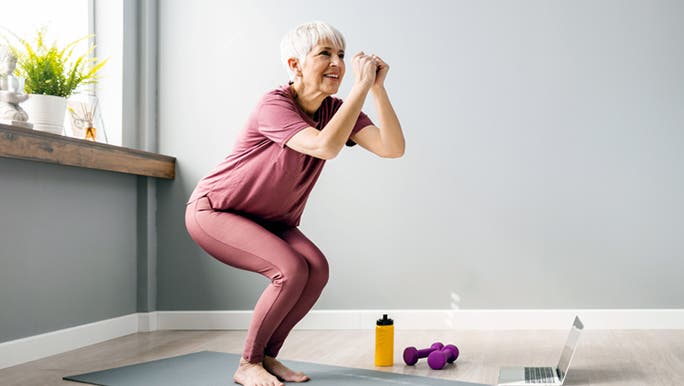  A senior woman wearing activewear is doing yoga on a grey mat