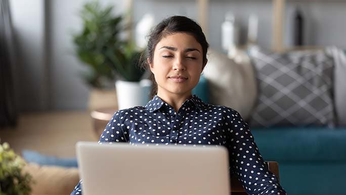A woman sitting in front of her laptop takes a break from work by practising mindfulness as part of her self-love week challenge. 