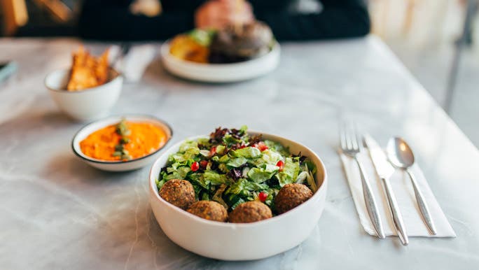 A falafel bowl with fresh green salad and carrot dip on a restaurant table