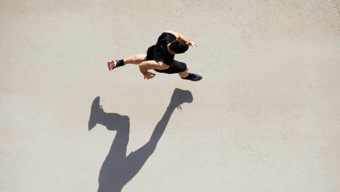 From above, a man runs on a concrete floor, both of his feet are off the ground so his shadow isn’t connected to him. It’s an impressive photo composition. 