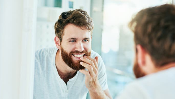 A man looks into the mirror at his teeth and wonders if there are any foods that can whiten them. 