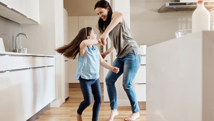 A woman and child are partaking in a mood boosting dance session. They are holding hands and smiling. 