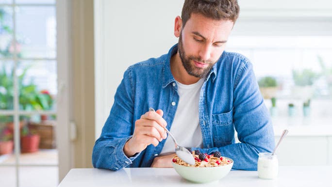 Man eating a healthy breakfast of muesli, berries and yogurt in his kitchen