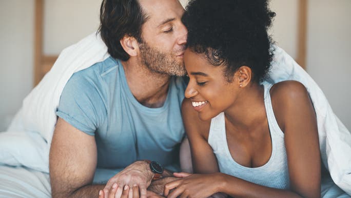 Man lying in bed with his partner kissing her affectionately on the forehead