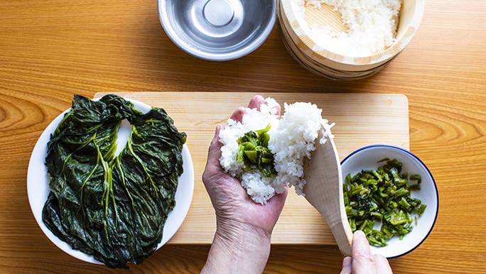 From above, someone prepares pickled leaves (T A K A N A) wrapped in rice. 