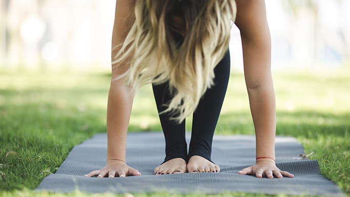 A woman is doing a deep back bend on the grass. Her hands are touching the ground on either side of her feet. 