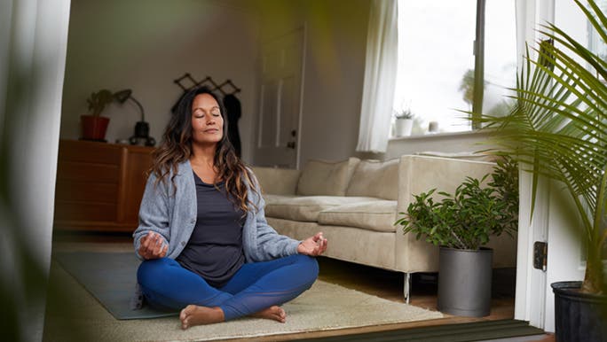 A woman meditates in front of an open door, the curtain is blowing in the wind. 