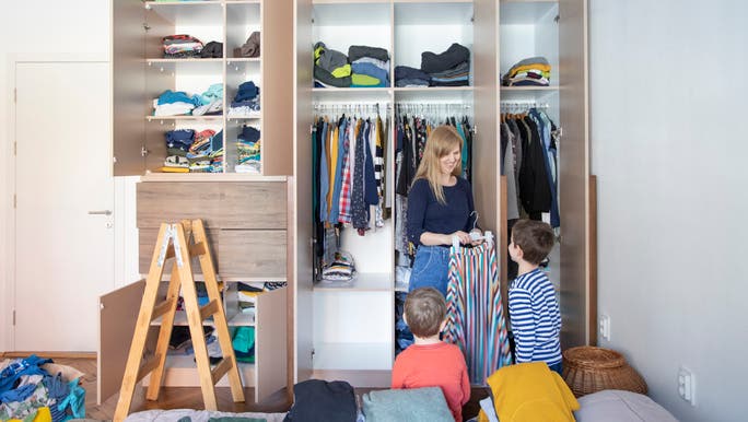 A young mother is smiling at two young boys as they tidy a children’s bedroom