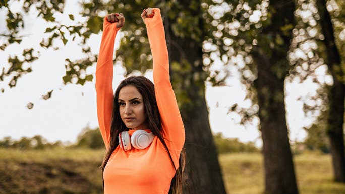Woman in orange activewear stretching before a run, she is warming up to prevent injury.