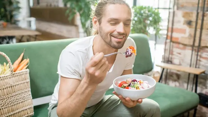 Young man sitting on a green couch eating a healthy fermented vegetable salad