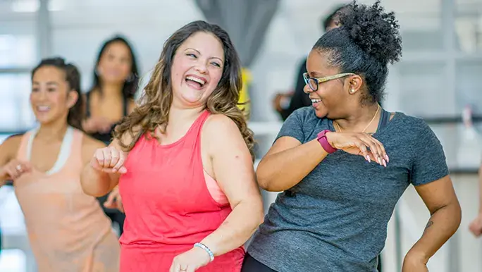 Two women are smiling at each other during the middle of a group fitness class.