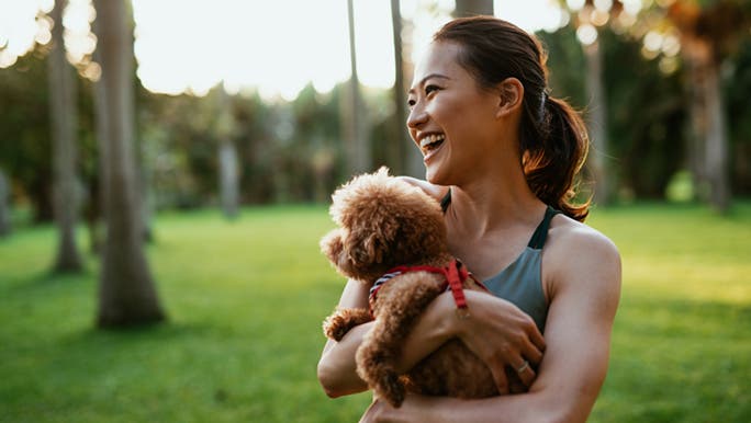 Focused on her fitness goals, a smiling woman holds a small dog in the park. 
