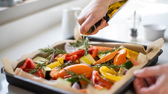 On a white kitchen bench, a tray of veggies fresh out of the oven is cooling. 