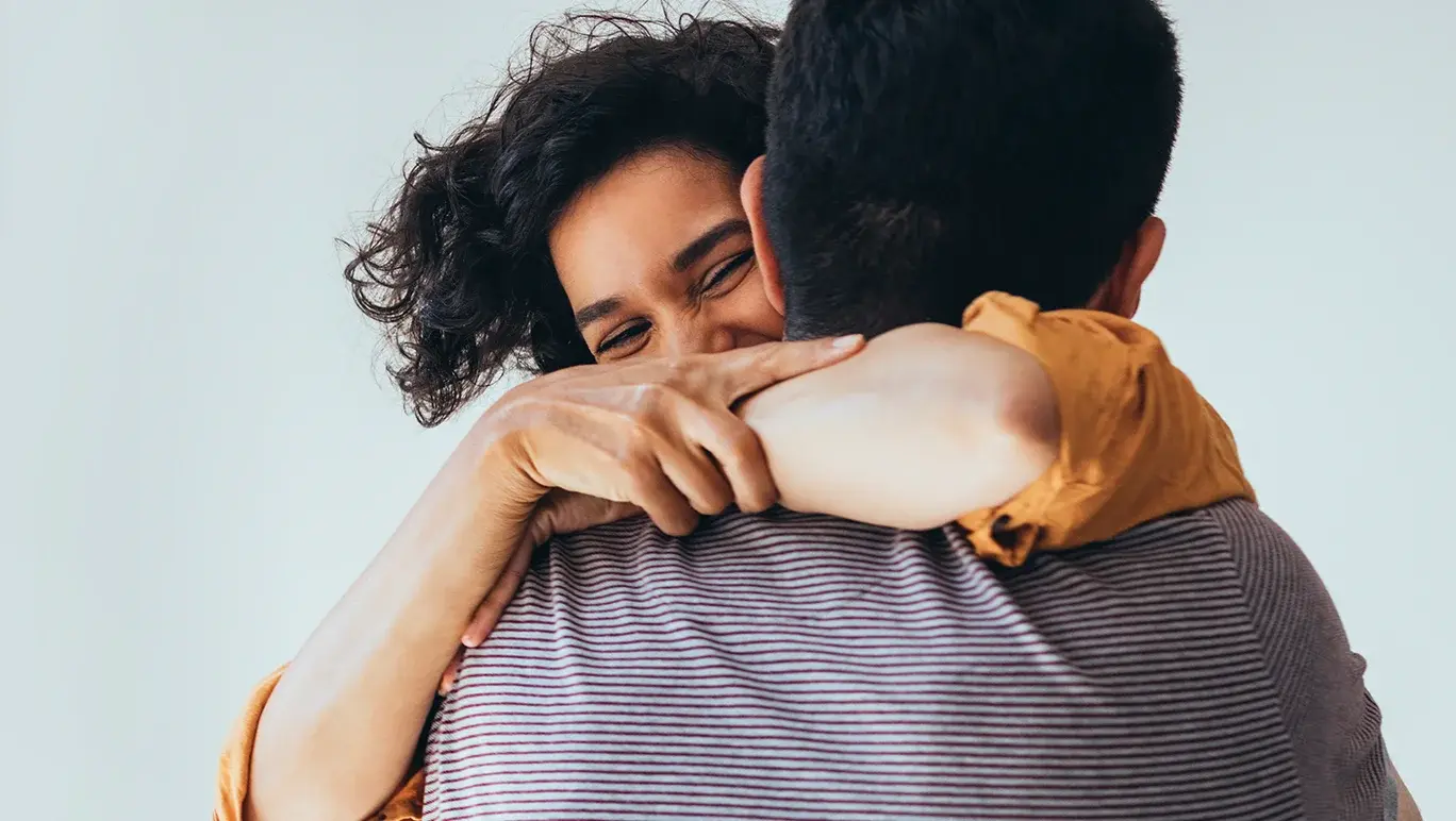 A woman lovingly embraces a man into a hug.
