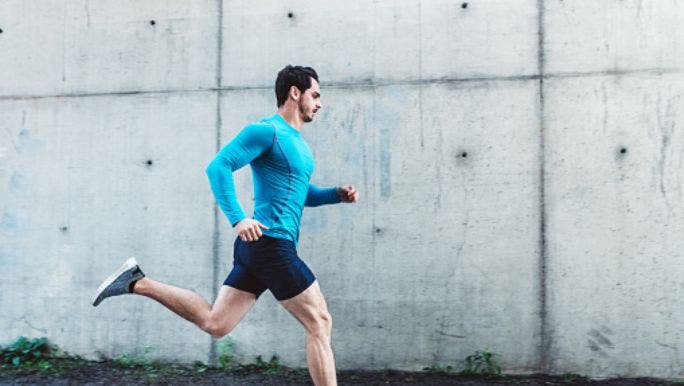 A young fit man wearing activewear is running outdoors on a concrete pavement