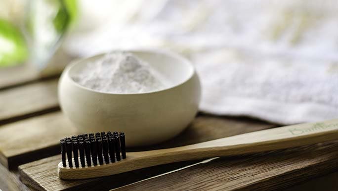 Natural toothbrush sits beside a bowl of tooth powder.