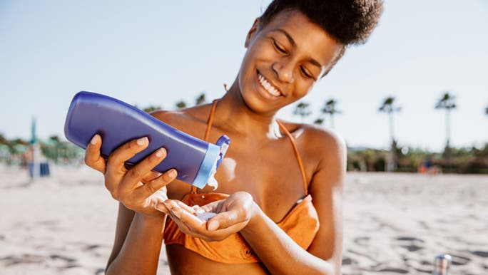 A woman at the beach is about to reapply sunscreen from a bottle because she knows how often you should reapply sunscreen. 